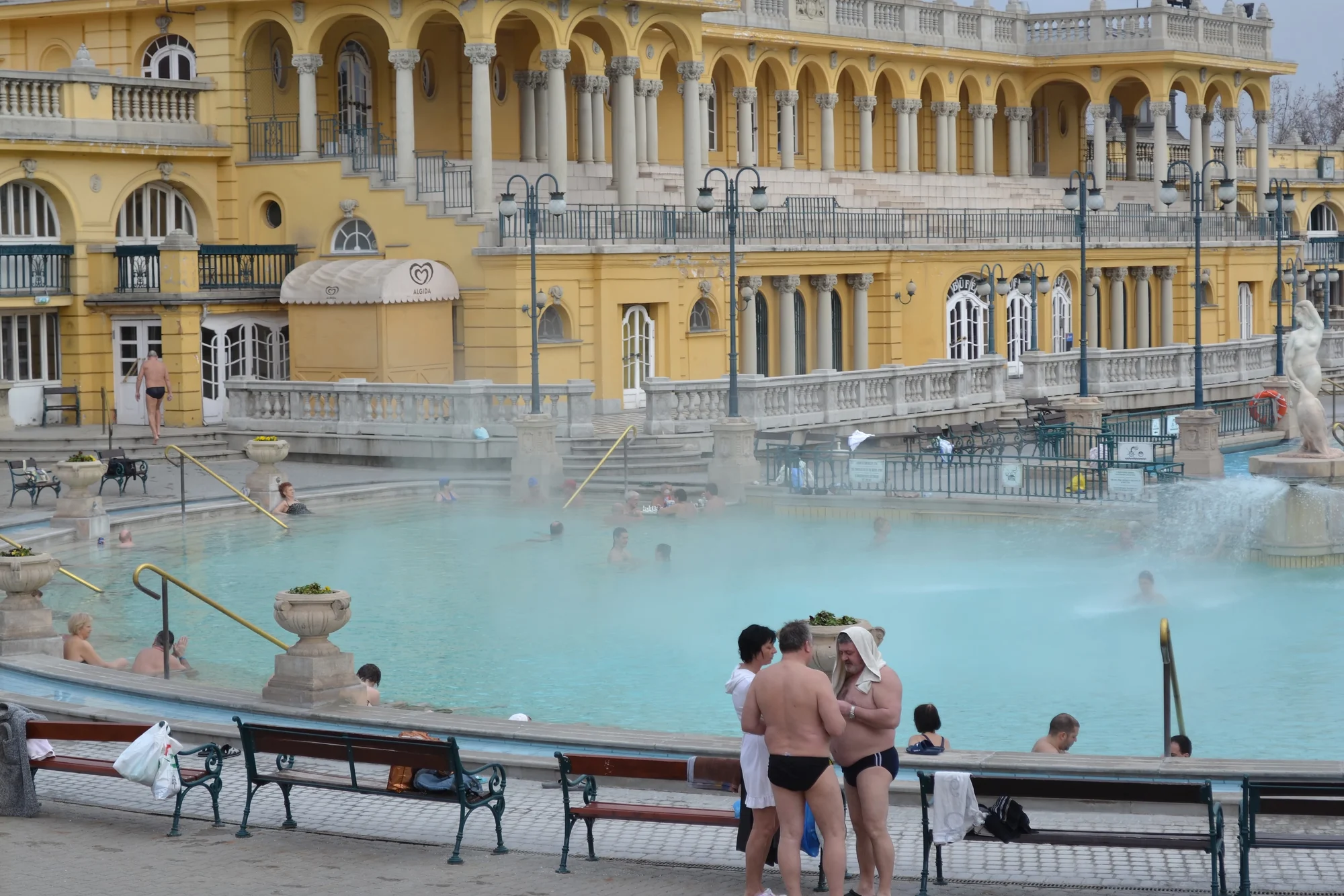 Outdoor thermal pool and yellow Neo-Baroque buildings at Széchenyi Thermal Bath in Budapest.